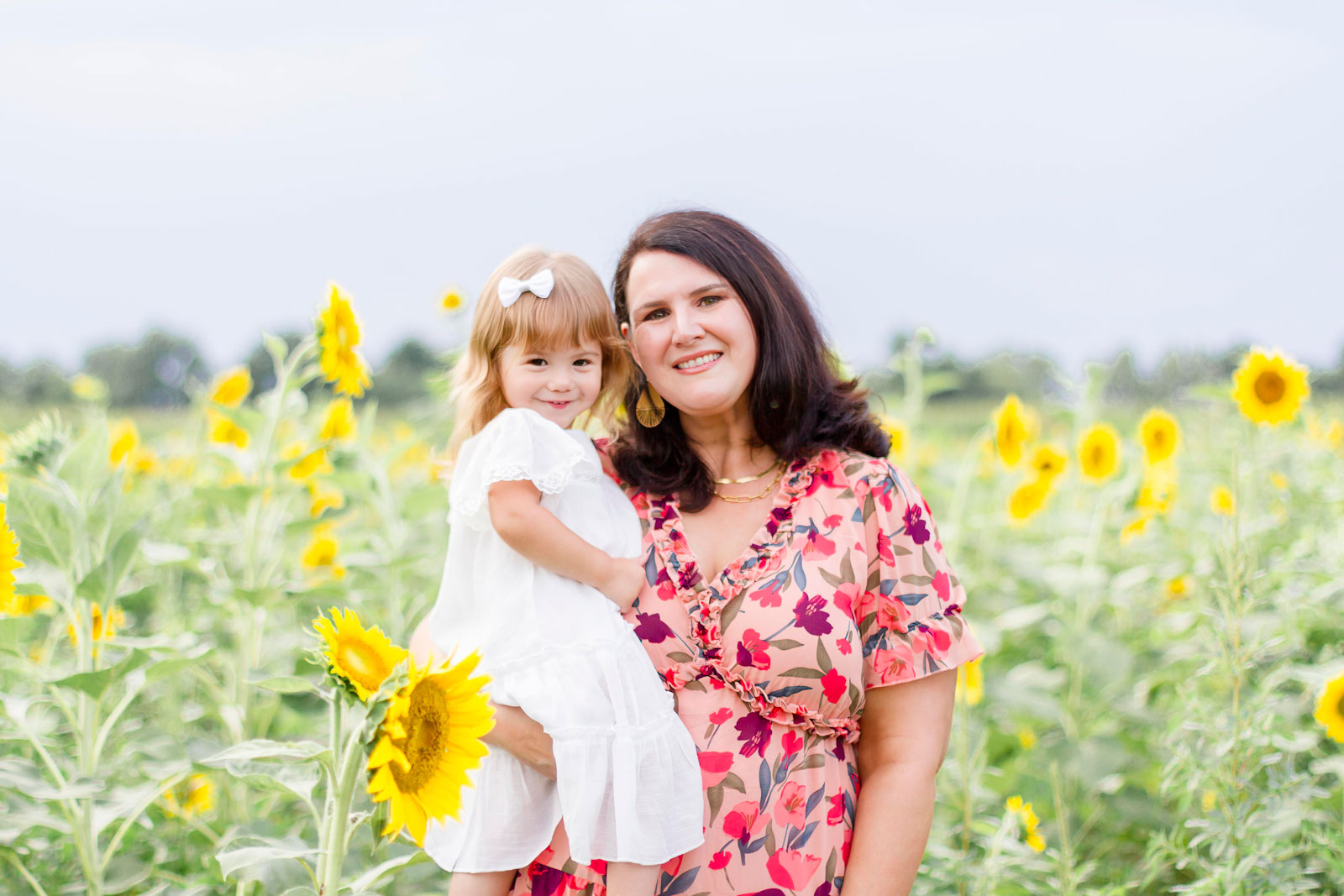 mom and her little girl looking at the camera smiling by the sunflowers at the sunflower field in Belcher, LA