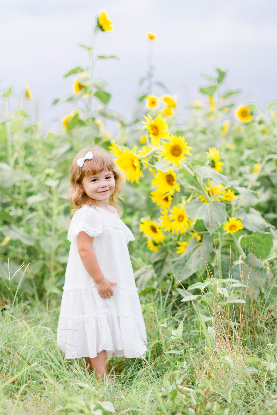 little girl smiling at the camera by the sunflowers at the sunflower field in Belcher, LA