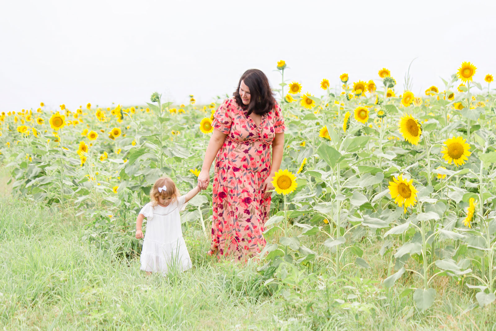 Mom and daughter walking along the sunflowers at the sunflower field in Belcher, LA