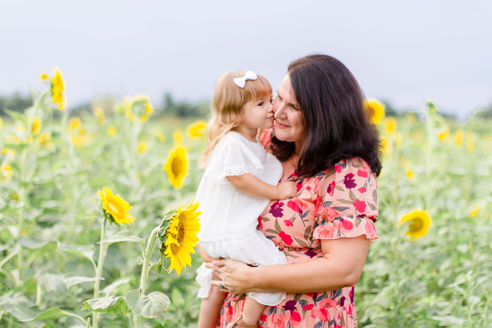 little girl giving her mom a kiss while mom holds her by the sunflowers at the sunflower field in Belcher, LA