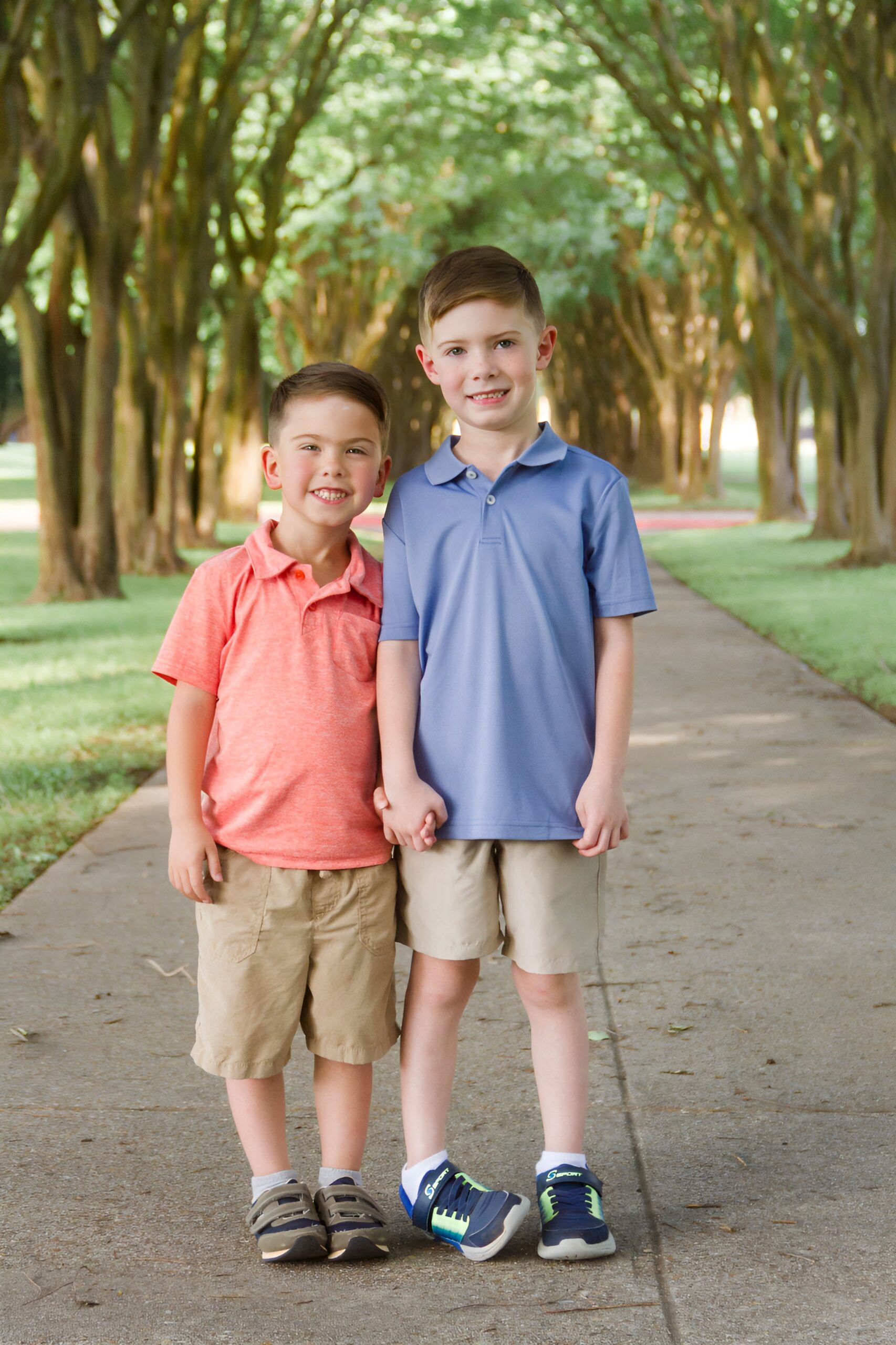 two brothers holding hands and standing next to each other on a pathway between trees outdoor for a family session in Shreveport LA