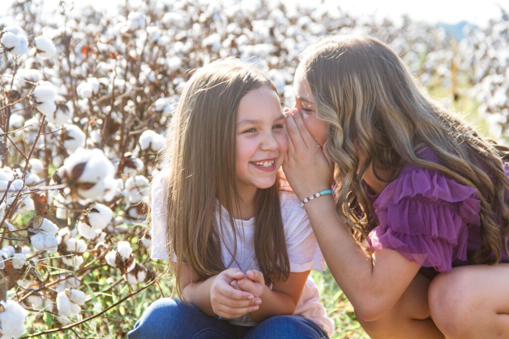 two little girls both sisters whispering in each other ears at the cotton field in belcher, la