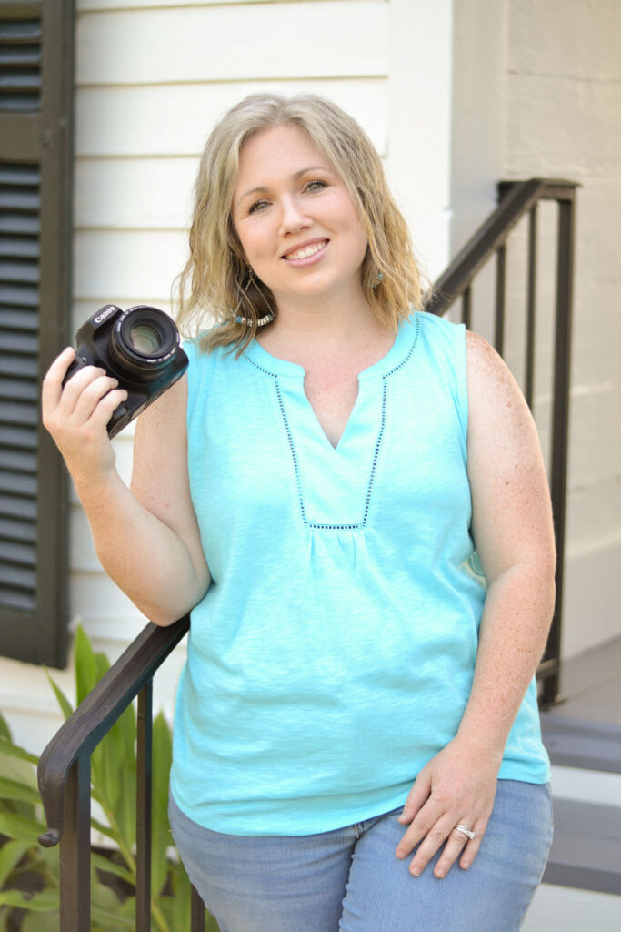 woman leaning again the rail of the steps while holding a canon camera smiling in Benton, Louisiana