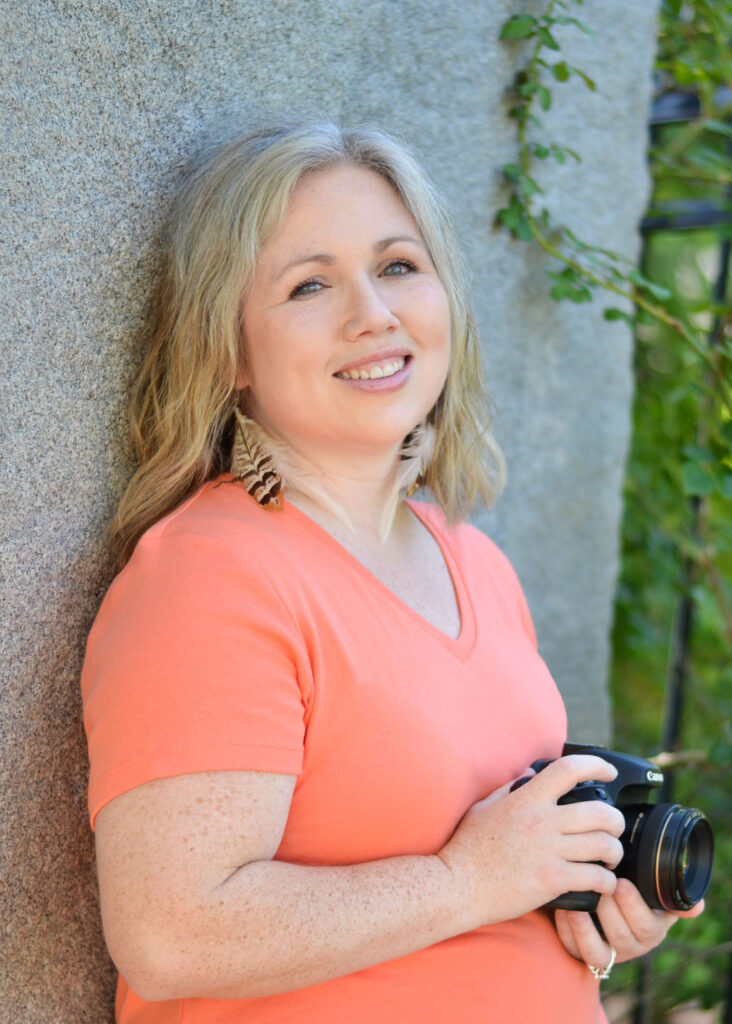 woman leaning against a concrete wall while holding her canon camera smiling at the camera in Benton, Louisiana