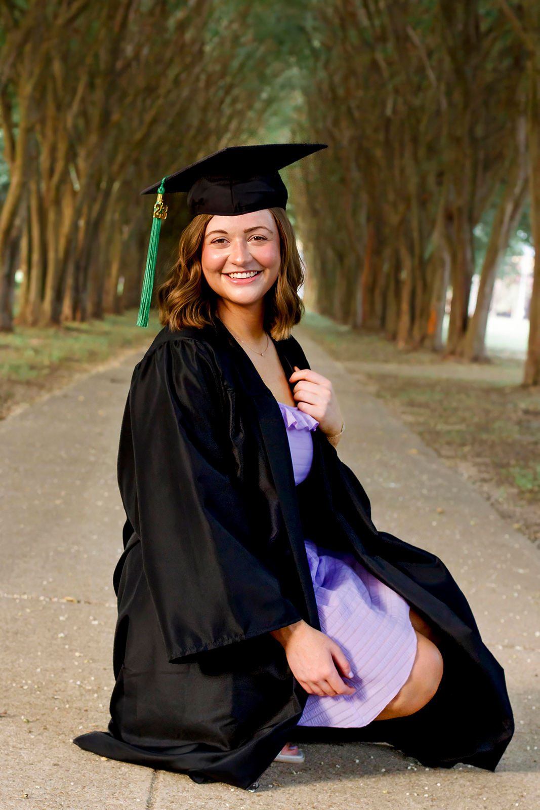 college grad med senior wearing black cap and gown while squatting on LSUS campus Shreveport LA