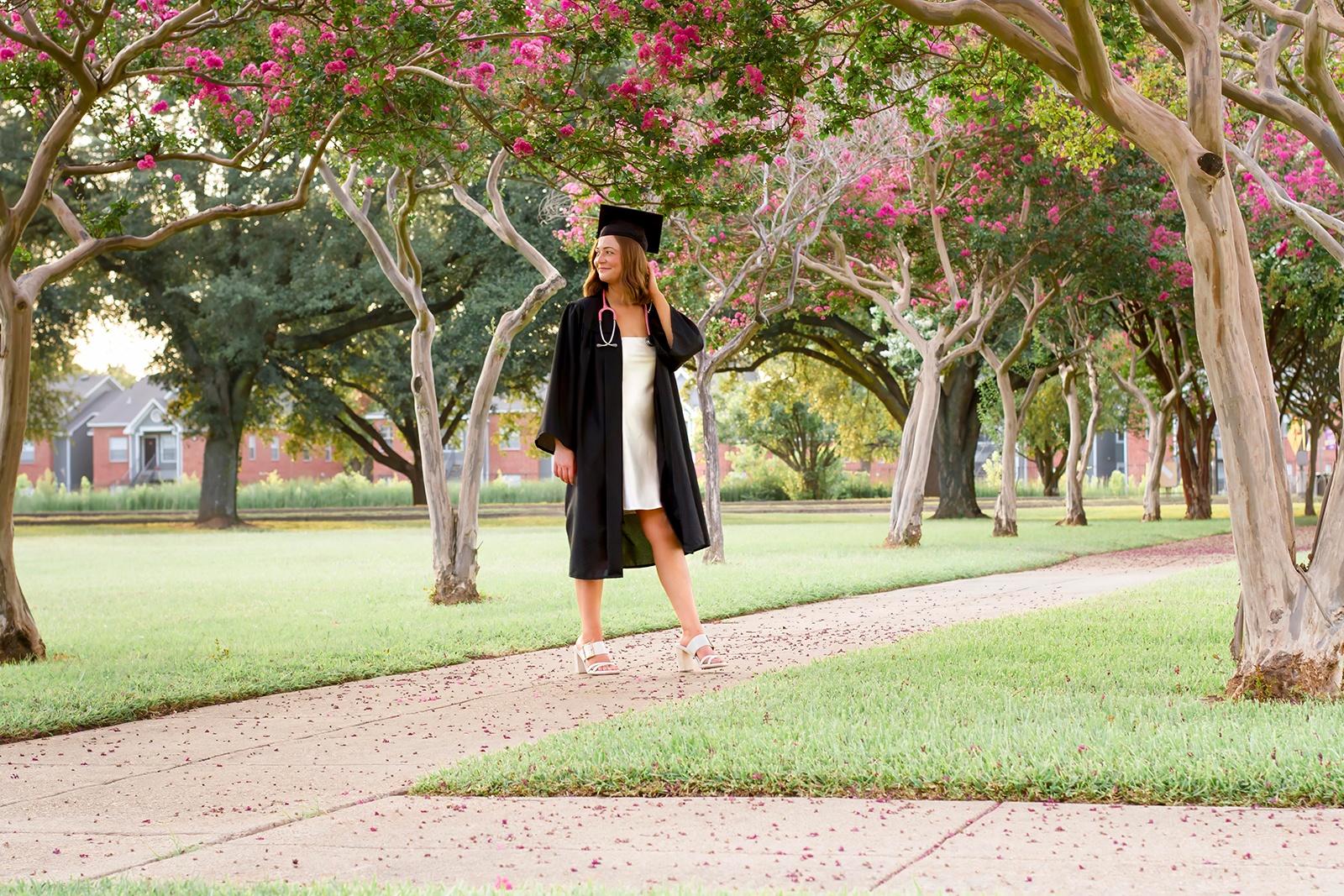 college grad med senior wearing black cap and gown near pink trees on LSUS campus Shreveport LA