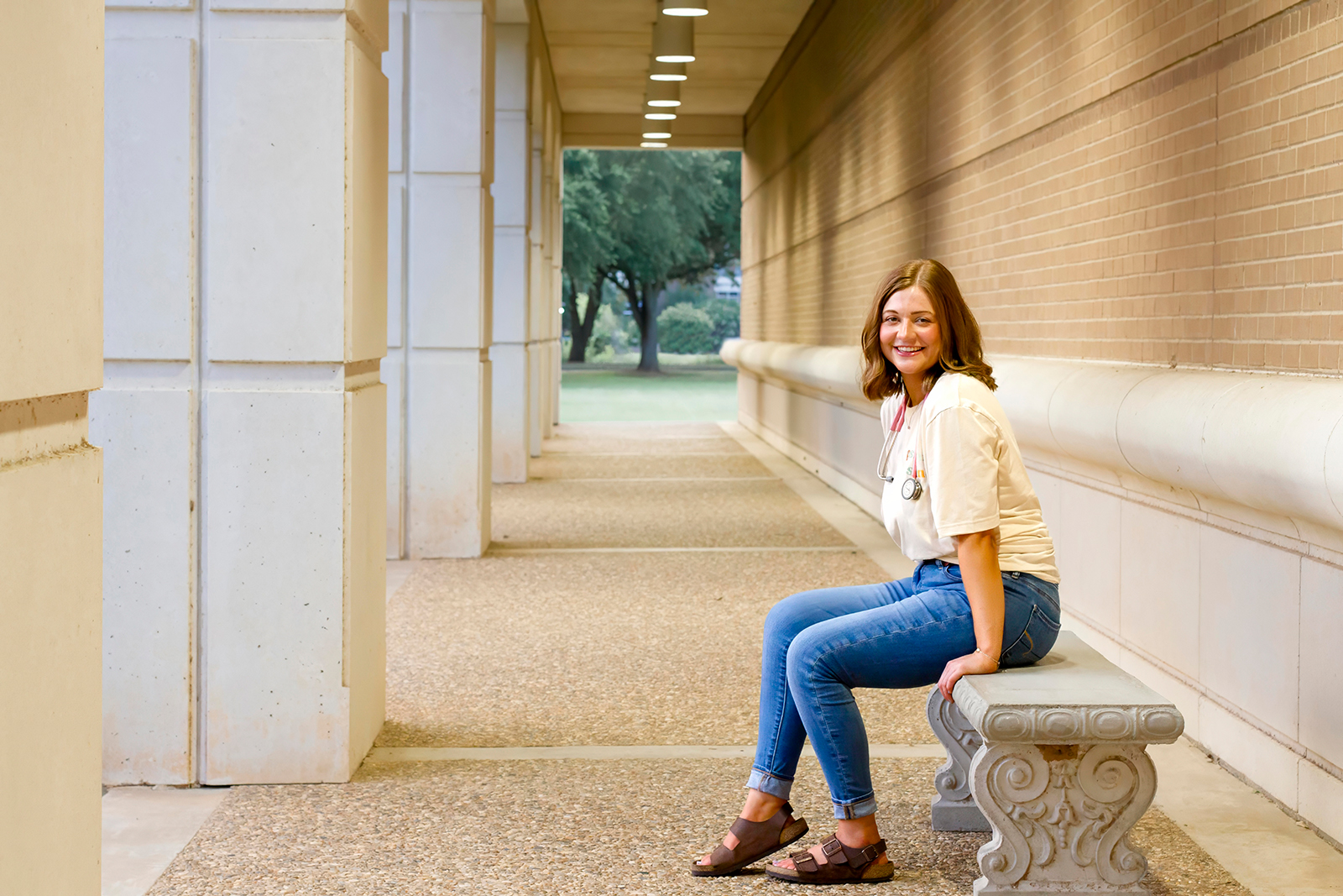 college grad med senior sitting on the bench down the hallways with pink stethoscope around her neck on LSUS campus Shreveport LA