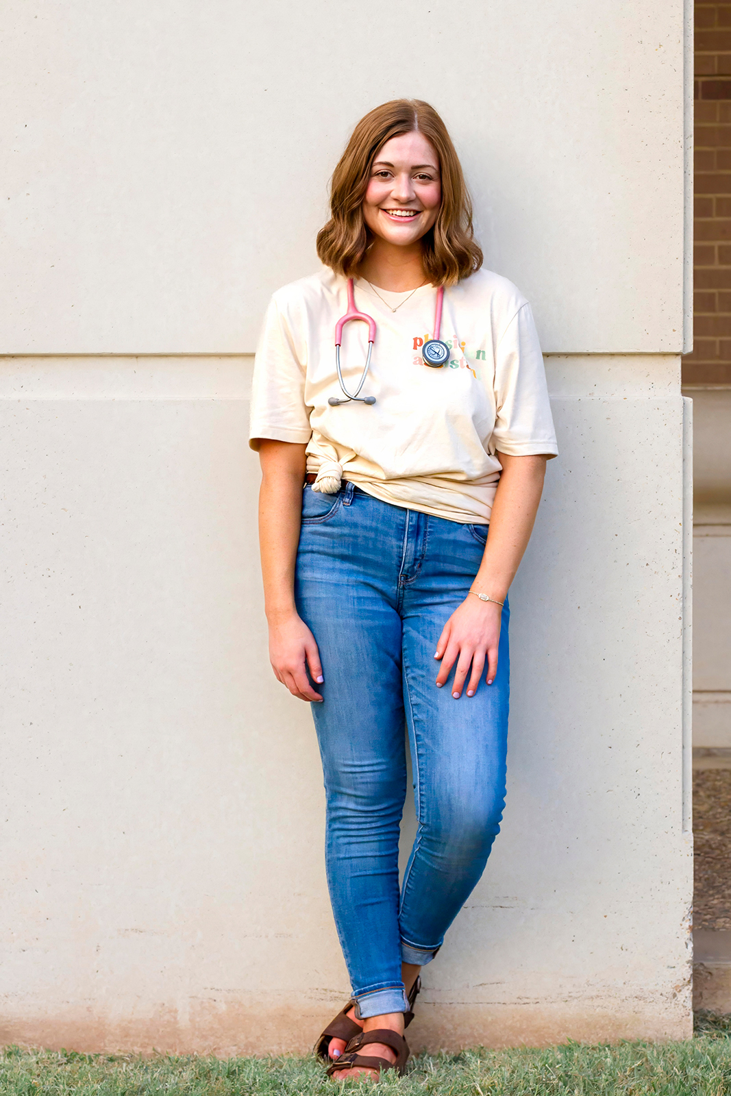 college grad med senior against the wall with pink stethoscope around her neck on LSUS campus Shreveport LA