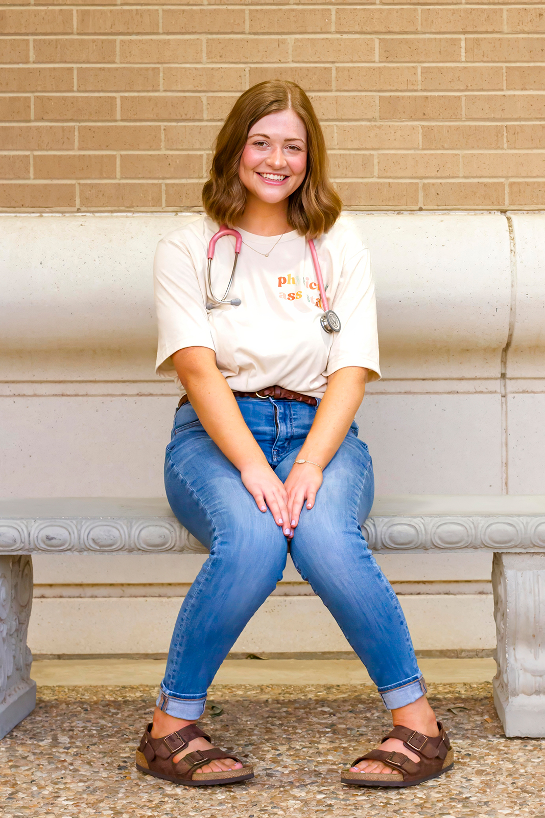 college grad med senior sitting on the bench with pink stethoscope around her neck on LSUS campus Shreveport LA