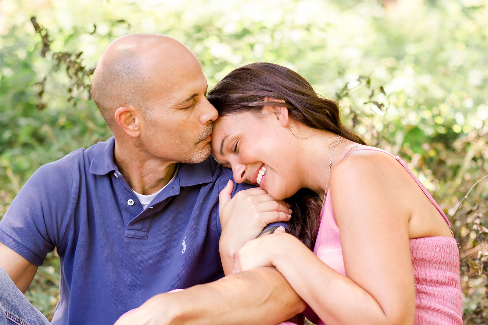 a couple leaning on each other man kissing woman forehead while she smiles in Shreveport, LA field of grass