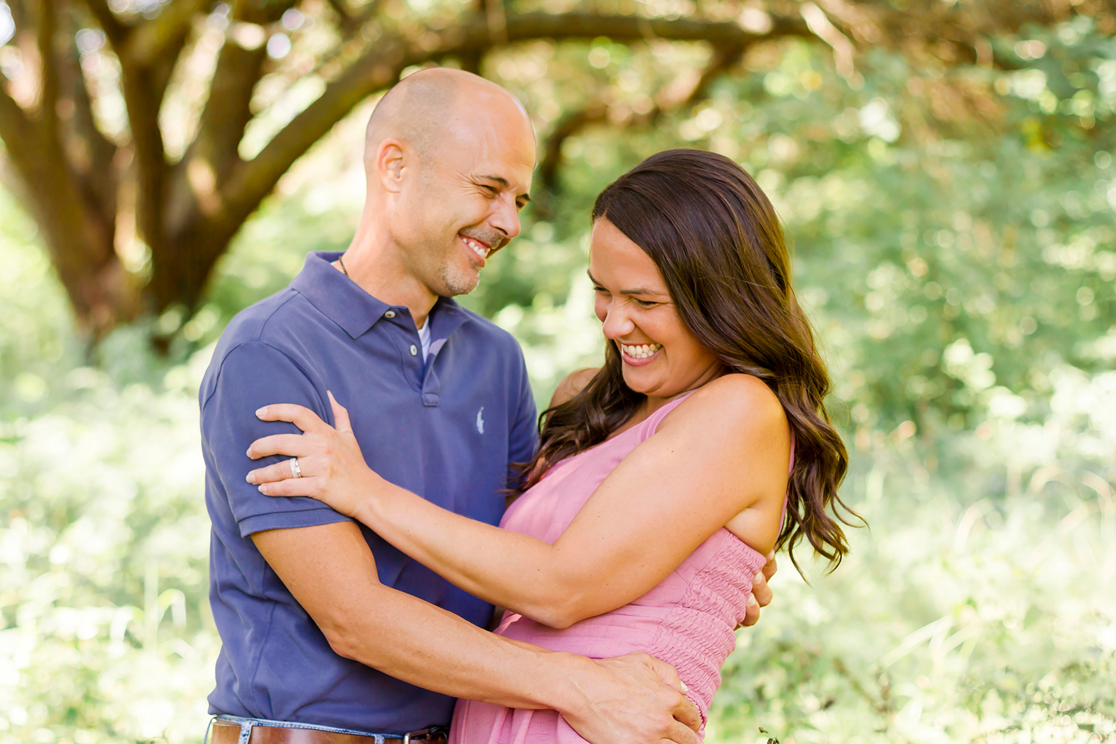 man and woman smiling and laughing as a couple while man holds woman in Shreveport, LA field of grass