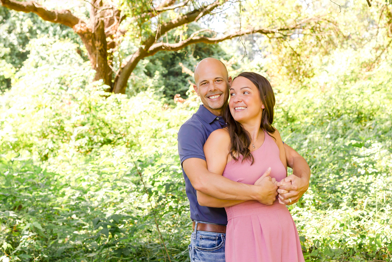 man wrapped his arms around woman while both are smiling as a couple in Shreveport, LA field of grass