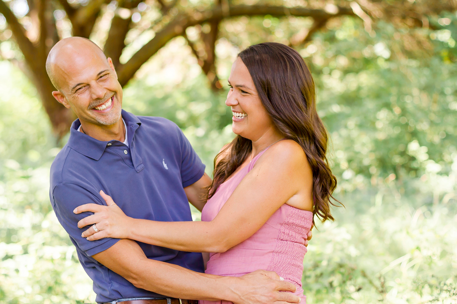 man and woman laughing and smiling as a couple while holding each other in Shreveport, LA field of grass