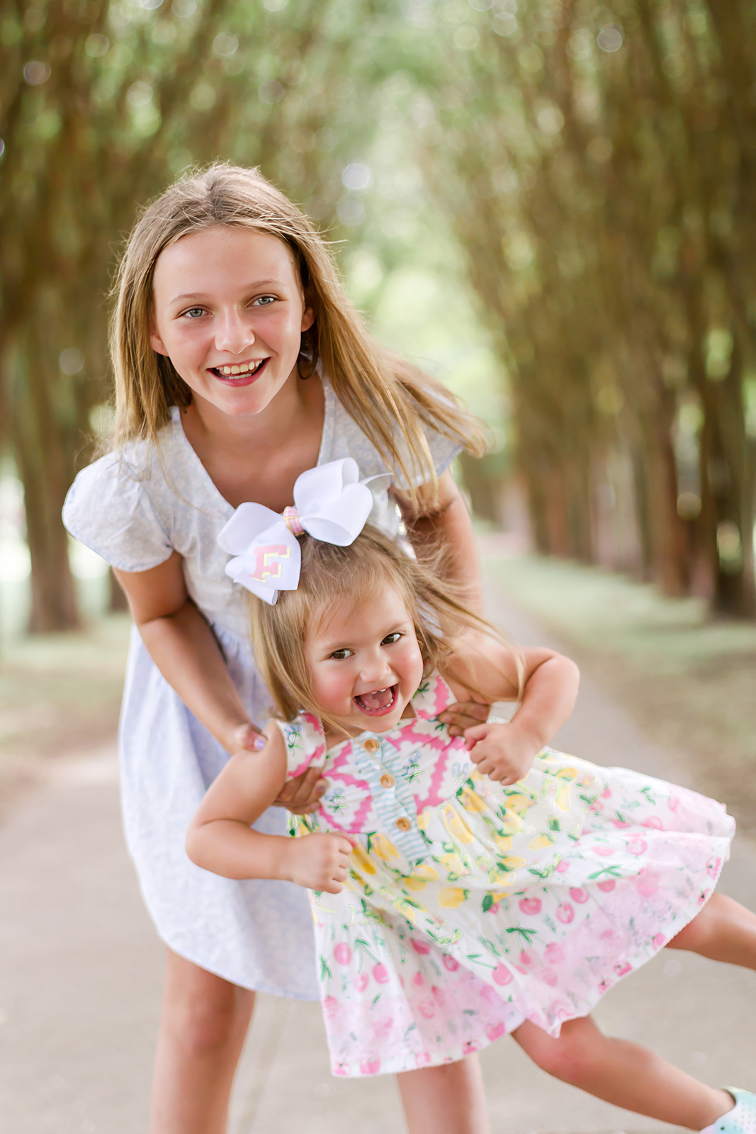 big sister swinging little sister while laughing on a pathway on LSUS campus in Shreveport, LA