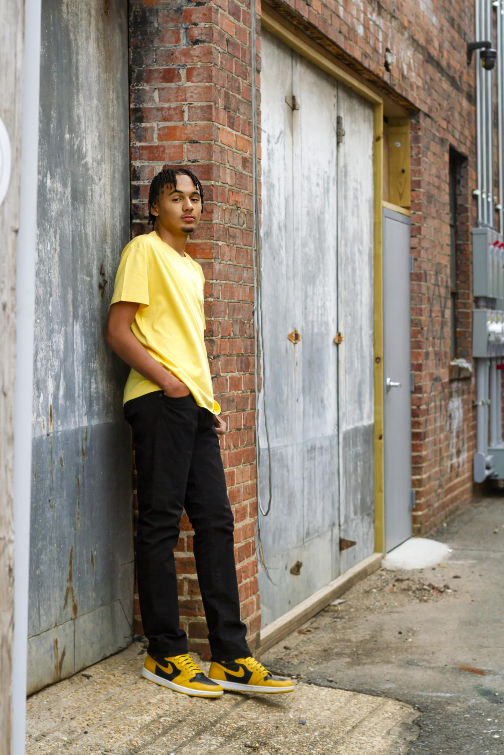 senior boy leaning against brick and metal in an alley in downtown Shreveport, LA